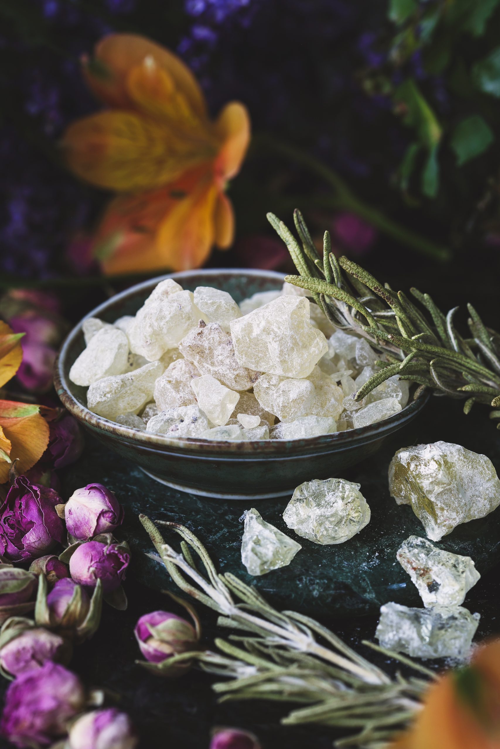 A small dish filled with copal resin with dried rosemary and rose buds nearby