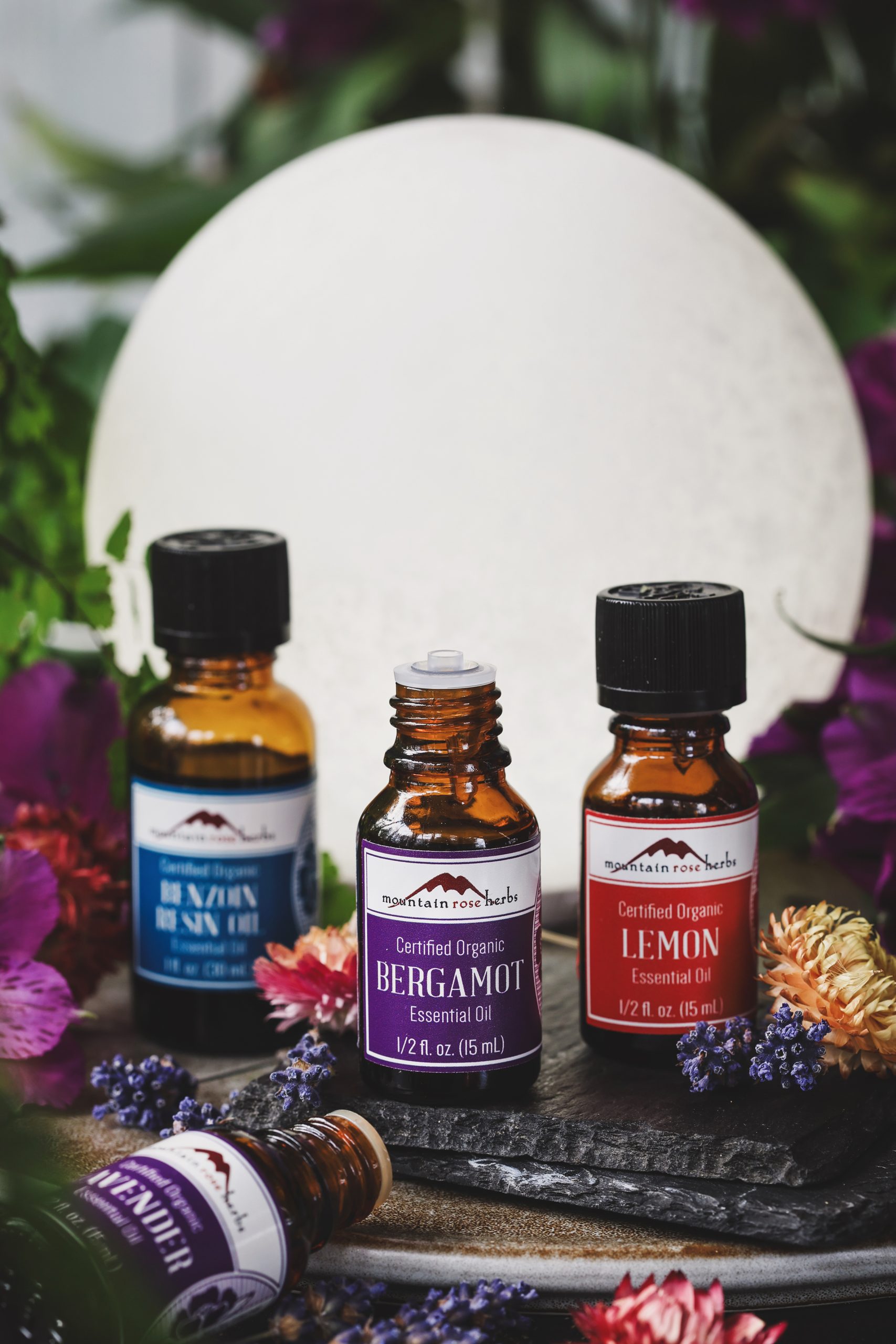 Bottles of bergamot, lemon, lavender, and benzoin essential oils with dried flowers around them