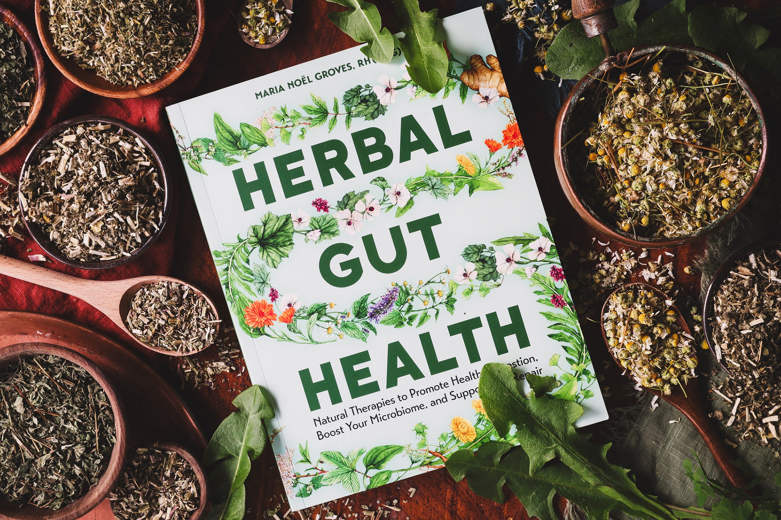 An overhead photo of Maria Noel Groves new book about Gut Health with bitter herbs around it